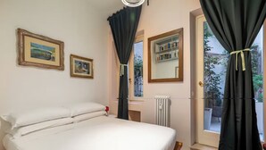 Un dormitorio con una cama grande, dos cuadros enmarcados, un radiador y una ventana con cortinas.