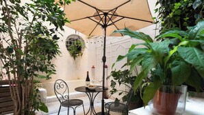 Un patio al aire libre con una mesa redonda, dos sillas, una botella de vino y una copa.
