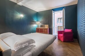 A bedroom with a bed, a nightstand, a red chair, and a window with a view of a building. - Via Giulia Serviced Apartment, Campo de' Fiori (Roma)