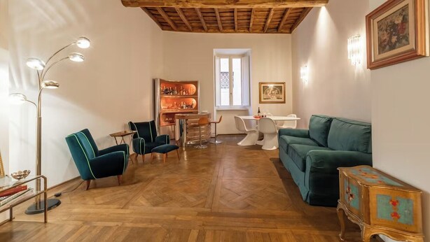 Una sala de estar con techo de madera, un sofá verde, una zona de comedor con mesa y sillas, y una barra con estantes llenos de botellas.