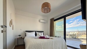 Un dormitorio con una cama grande, una mesita de noche, una lámpara colgante y vistas a la ciudad a través de un ventanal.