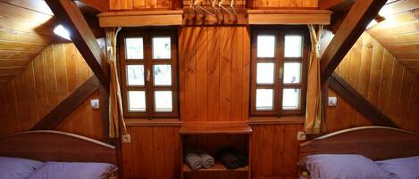 Una habitación cálida de cabaña de madera con dos camas, un estante con toallas y una ventana con cortinas.