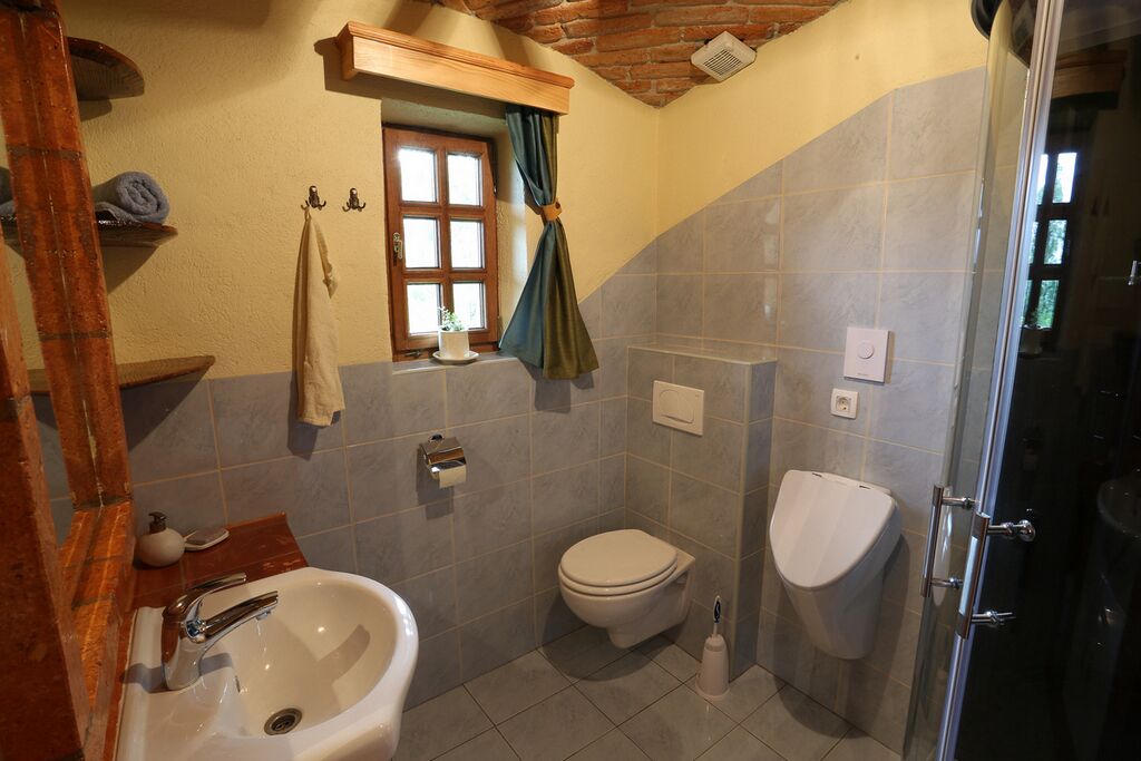 Een badkamer met een wastafel, toilet en bidet, een raam met gordijnen, en een douchegedeelte.