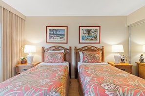 Een hotelkamer met twee bedden, elk met een bloemenprint sprei, houten hoofdborden en nachtlampjes. Boven de bedden hangen twee ingelijste foto's.