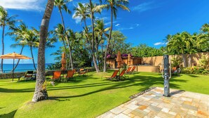 Un espacio tropical al aire libre con palmeras, un patio de piedra y sillas de descanso.