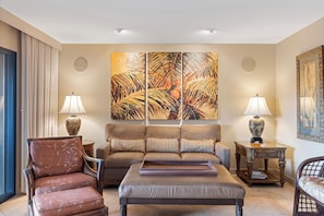 A spacious room with a large bed, a sitting area with a chair and a small table, and a large painting on the wall. - Wailea Elua #2107 - Spacious, Stylish & Just Moments from Wailea Beach (Wailea, Maui)