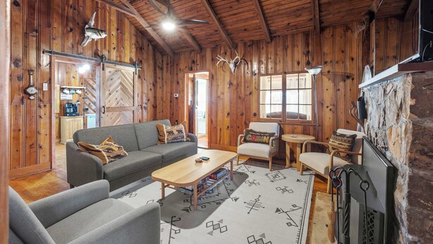A rustic cabin interior with wooden walls, a sofa, a coffee table, a fireplace, and a dining area. - Rockaway Retreat (Rockaway Beach)