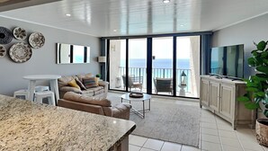 A modern living room with a large sliding glass door leading to a balcony with a view of the sea.