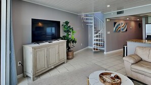A modern living room with a flat-screen TV, a staircase, a dining area, and a sofa.