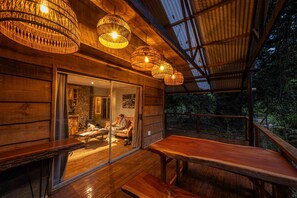 Eine Holzhütte mit Glastür, die in ein gemütliches Interieur führt, einer Holzterrasse und hängenden Korblampen.