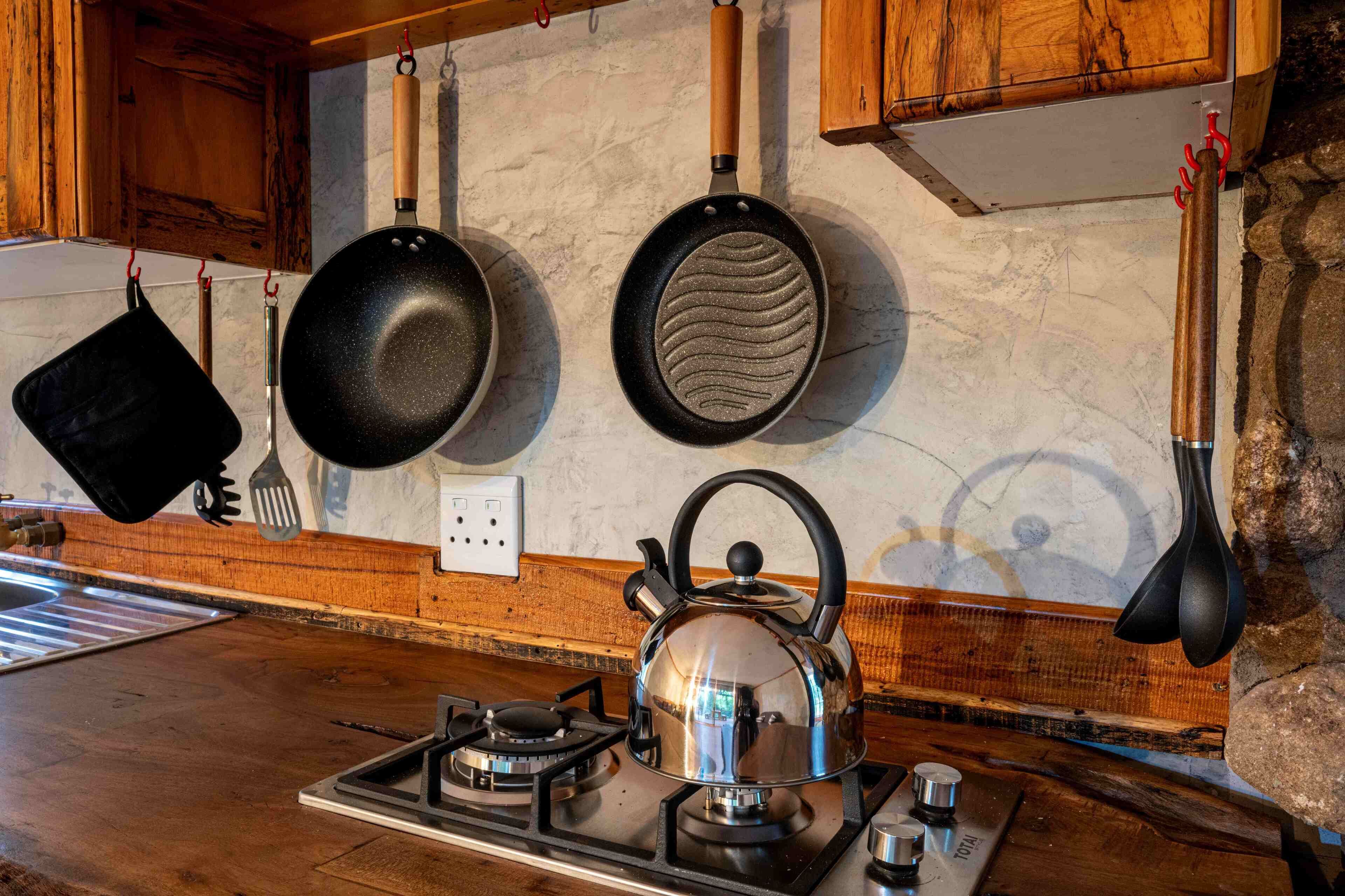 Une cuisine équipée d’une cuisinière à gaz, d’une bouilloire et d’ustensiles de cuisine suspendus.