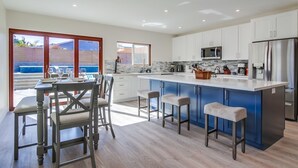 Una cocina moderna con una isla grande, armarios blancos y un comedor con mesa y sillas.