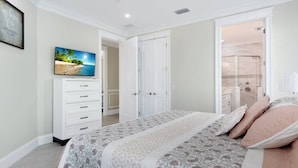 Une chambre à coucher avec un lit, une télévision, une armoire et une salle de bain visible à travers une porte ouverte.