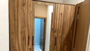 A wooden wardrobe with a mirrored door, a tiled floor, and a visible bathroom in the background. - Luxury studio (Lomé)