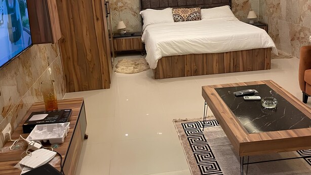 A modern bedroom with a large bed, wooden furniture, a flat-screen TV, and a coffee table. - Luxury studio (Lomé)