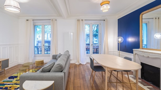 Un salon moderne comprenant un canapé, une table à manger et des chaises, de grandes fenêtres avec des rideaux et une cheminée.