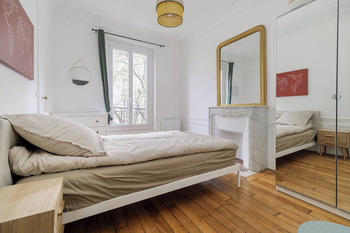 Une chambre à coucher avec un lit, un miroir, une commode et une fenêtre avec des rideaux.