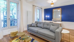 Un salon moderne avec un canapé gris, une table basse ronde, un petit tabouret et un grand miroir sur un mur bleu.