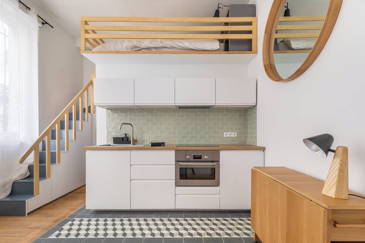 Une cuisine compacte dotée d’un four encastré, d’un banc en bois et d’un escalier menant à un lit en mezzanine.