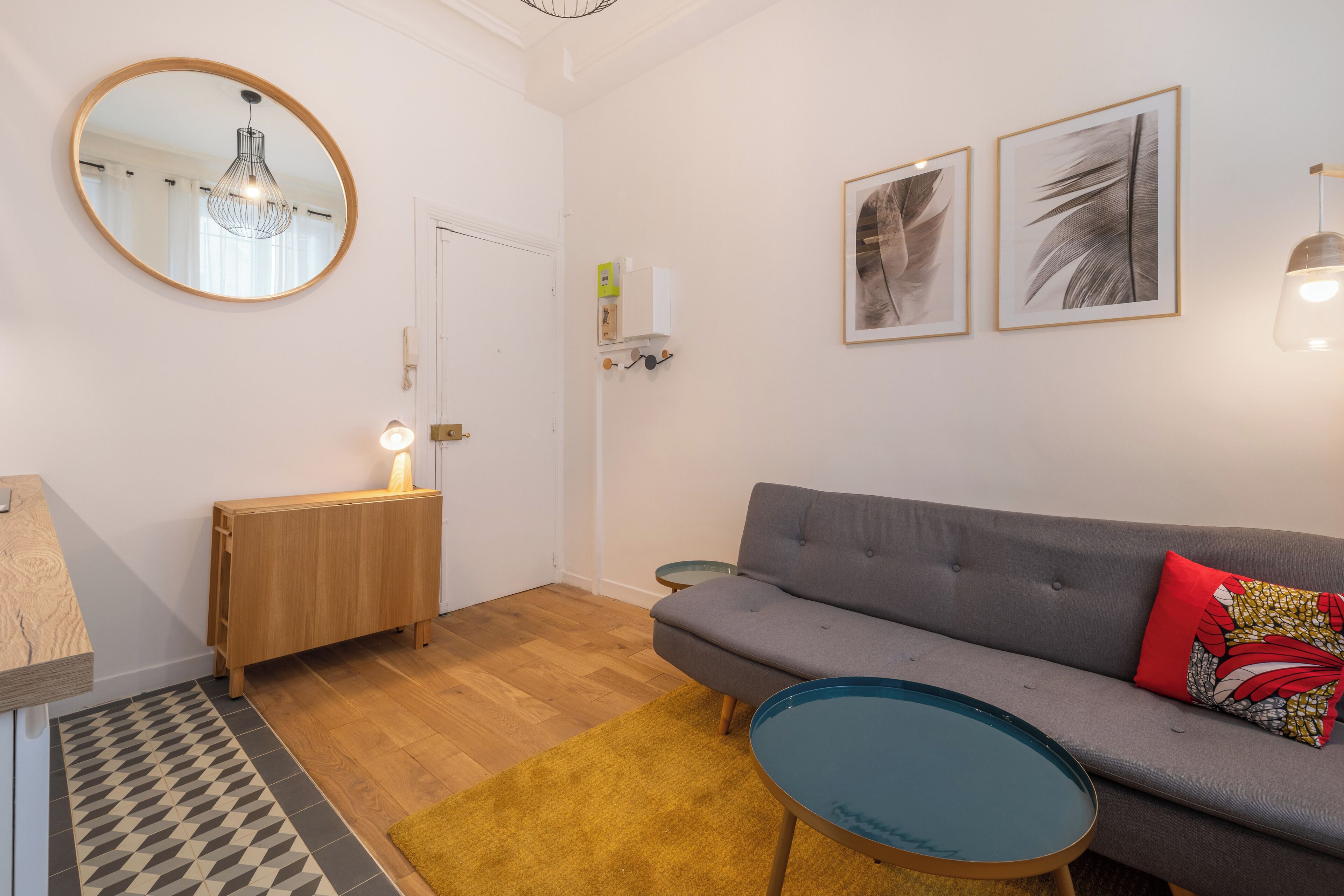 A modern living room with a grey sofa, a round mirror, and two framed artworks on the wall.