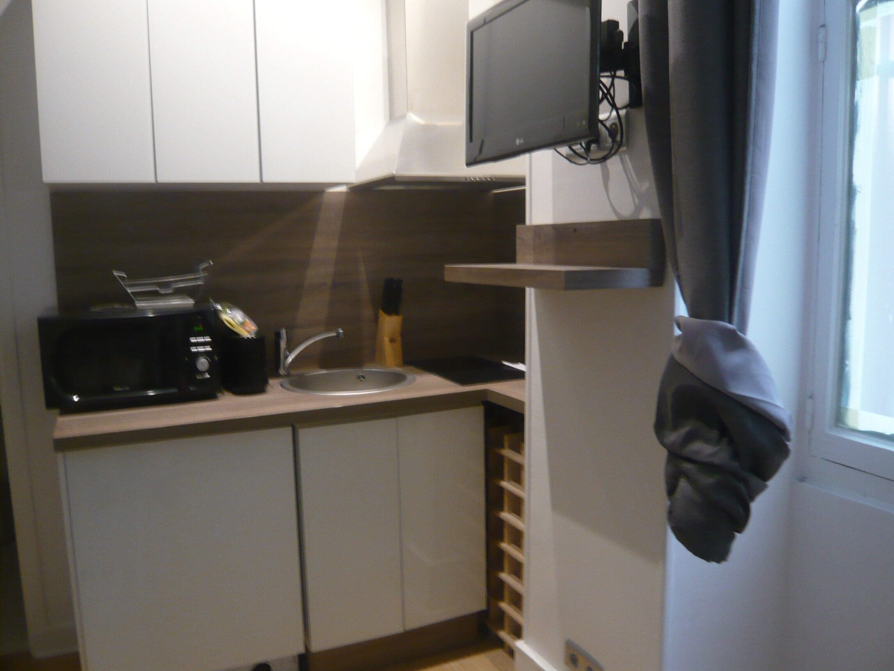 A small kitchenette with a microwave, sink, and a TV mounted on the wall.