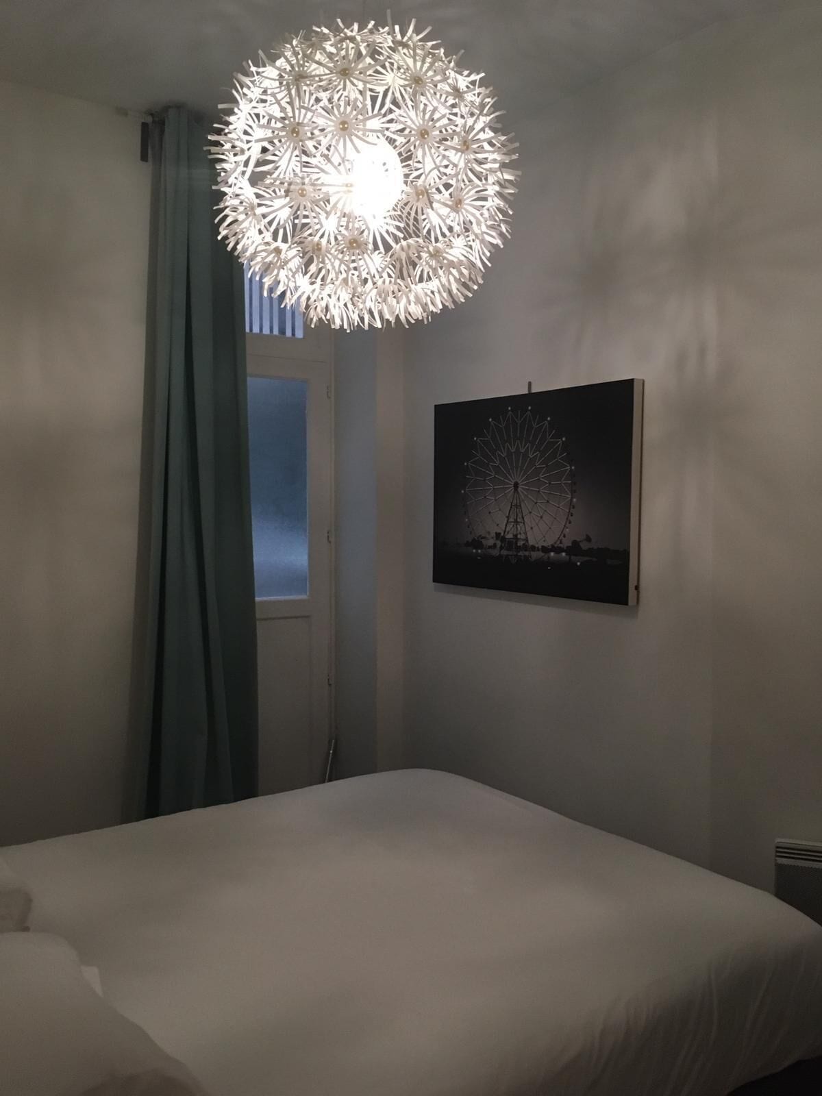 A bedroom with a bed, a wall-mounted picture of a Ferris wheel, and a unique chandelier.