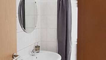 Un baño con un lavamanos blanco, un espejo redondo y una cortina de ducha.