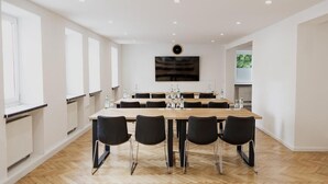 Une salle de conférence moderne, dotée d’une longue table, de chaises noires et d’un téléviseur à écran plat fixé au mur.
