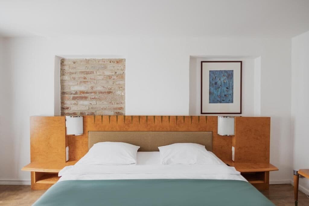 Une chambre d’hôtel avec une tête de lit en bois, un mur en briques et une œuvre d’art encadrée.