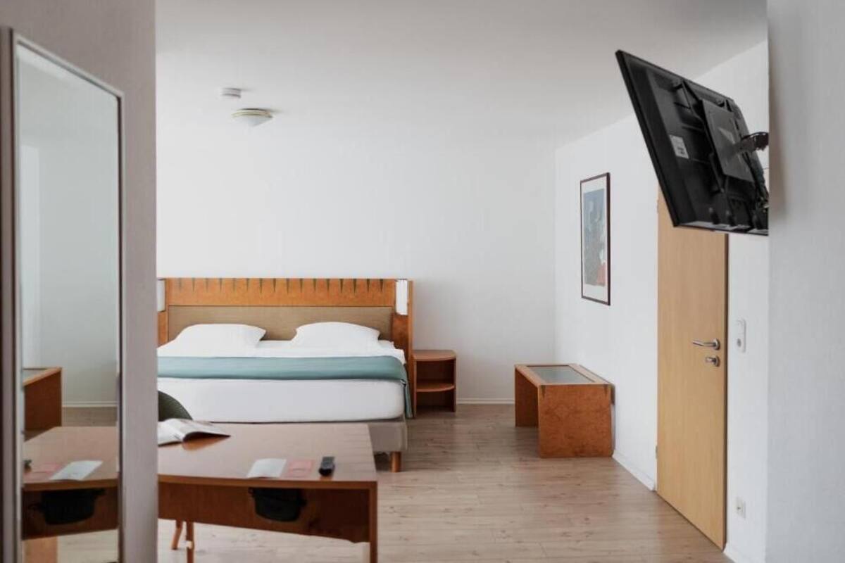 A hotel room with a wooden bed, a desk, a wardrobe, and a mounted TV.