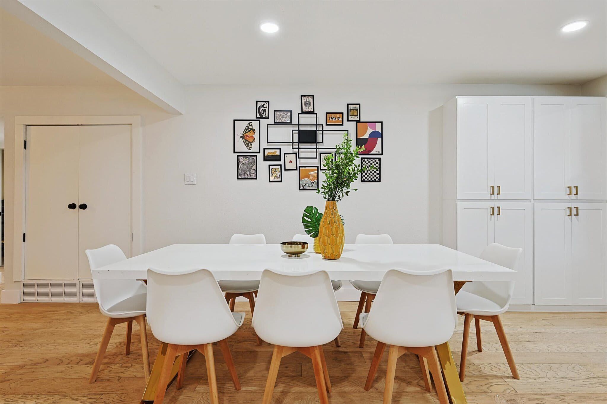 A dining area with a white table, white chairs, and a decorative wall piece.