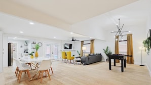 Amplia sala de estar con mesa de comedor, sillas amarillas, sofá y mesa de futbolín, además de ventilador de techo.