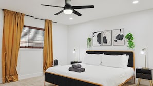 Un dormitorio moderno con cama, ventilador de techo, ventana con persianas y decoración en la pared.
