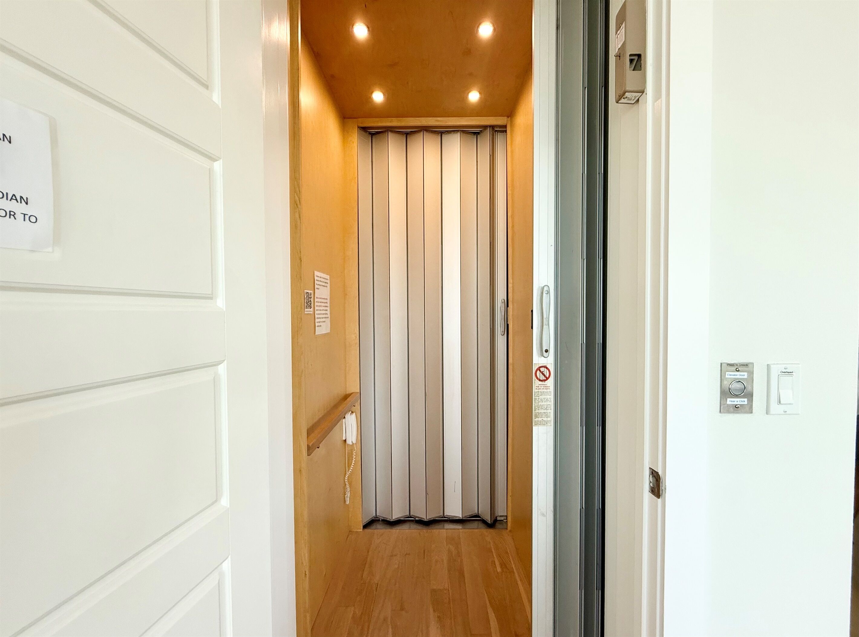 Un couloir étroit doté d’un plancher en bois, d’une porte coulissante à l’intérieur blanc et d’un interphone fixé au mur.