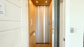 Un couloir étroit doté d’un plancher en bois, d’une porte coulissante à l’intérieur blanc et d’un interphone fixé au mur.