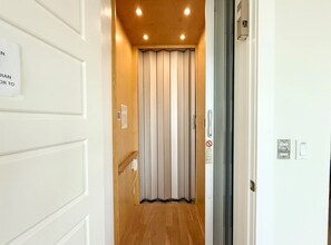 A narrow hallway with a wooden floor, a sliding door with a white interior, and a wall-mounted intercom. - Gulf Views 🌊 | Elevator 🏡 | 1 Minute to Beach 🌴| Heated Pool & Spa 🌅Sunsets (Anna Maria)