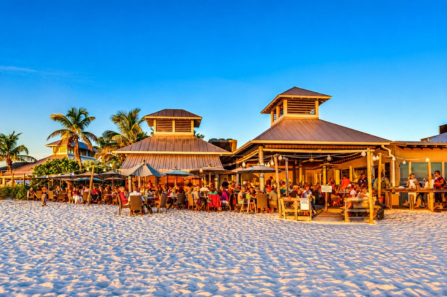 A beachfront restaurant with outdoor seating and a covered patio area.