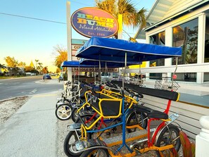 A row of colorful pedal boats parked outside a building with a sign reading "Beach Bums Island Attitude."