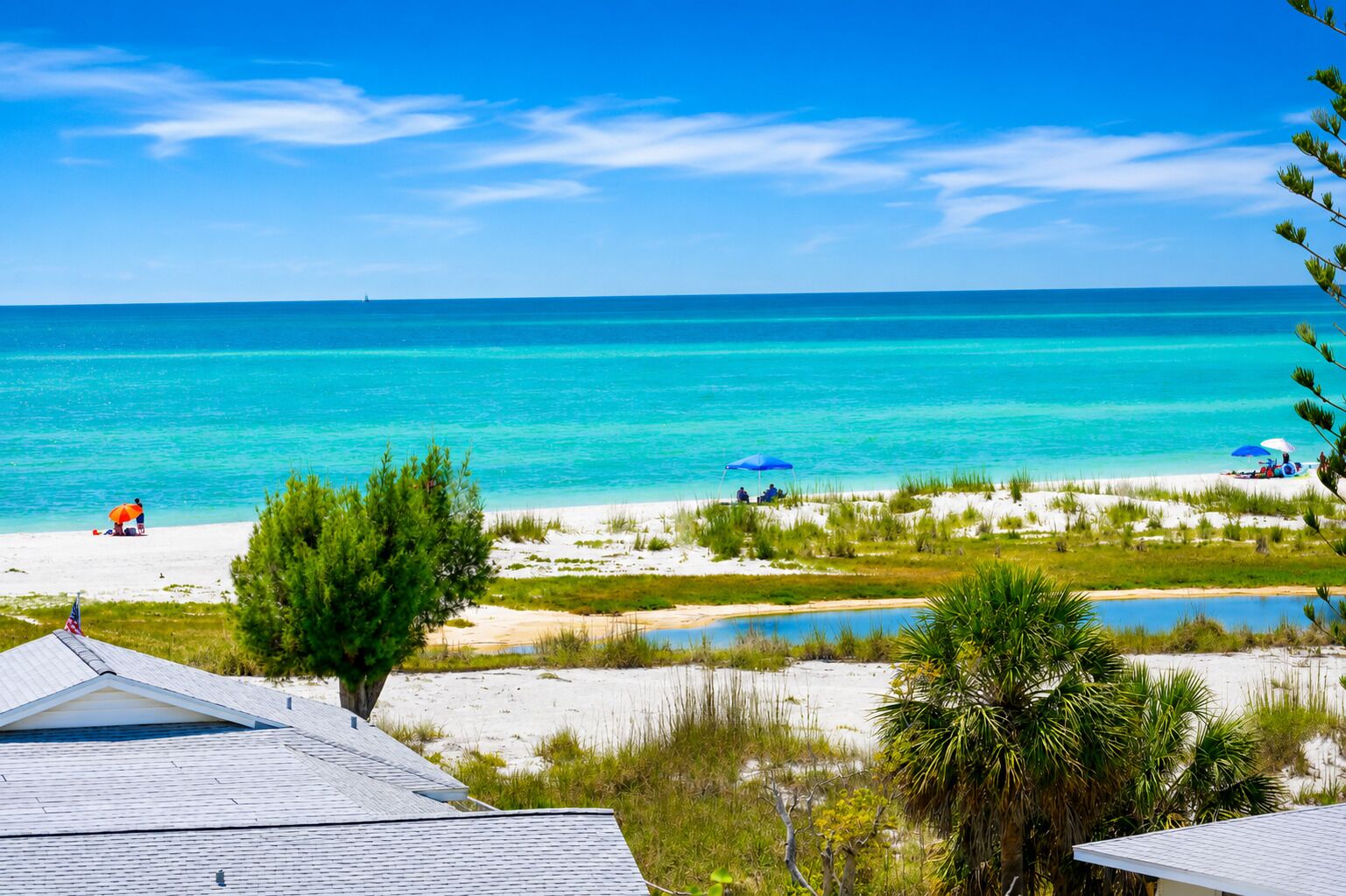 A beach with clear turquoise water, a sandy shore, and a few umbrellas.