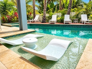 A poolside area with lounge chairs and a small table. - Shore to Please | Gulf Views 🌊 Elevator | Beach 1 Min 🌴 | Heated Pool & Spa 🌅 (Anna Maria)