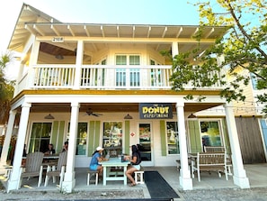 A two-story building with a balcony, a sign reading "The Donut Experiment," and outdoor seating with tables and chairs. - Gulf Views 🌊 | Elevator 🏡 | 1 Minute to Beach 🌴| Heated Pool & Spa 🌅Sunsets (Anna Maria)