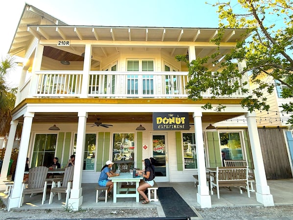 A two-story building with a balcony, a sign reading "The Donut Experiment," and outdoor seating with tables and chairs.