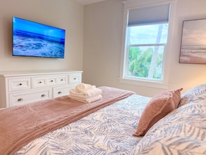 A bedroom with a bed, a TV on the wall, a window, and a dresser.