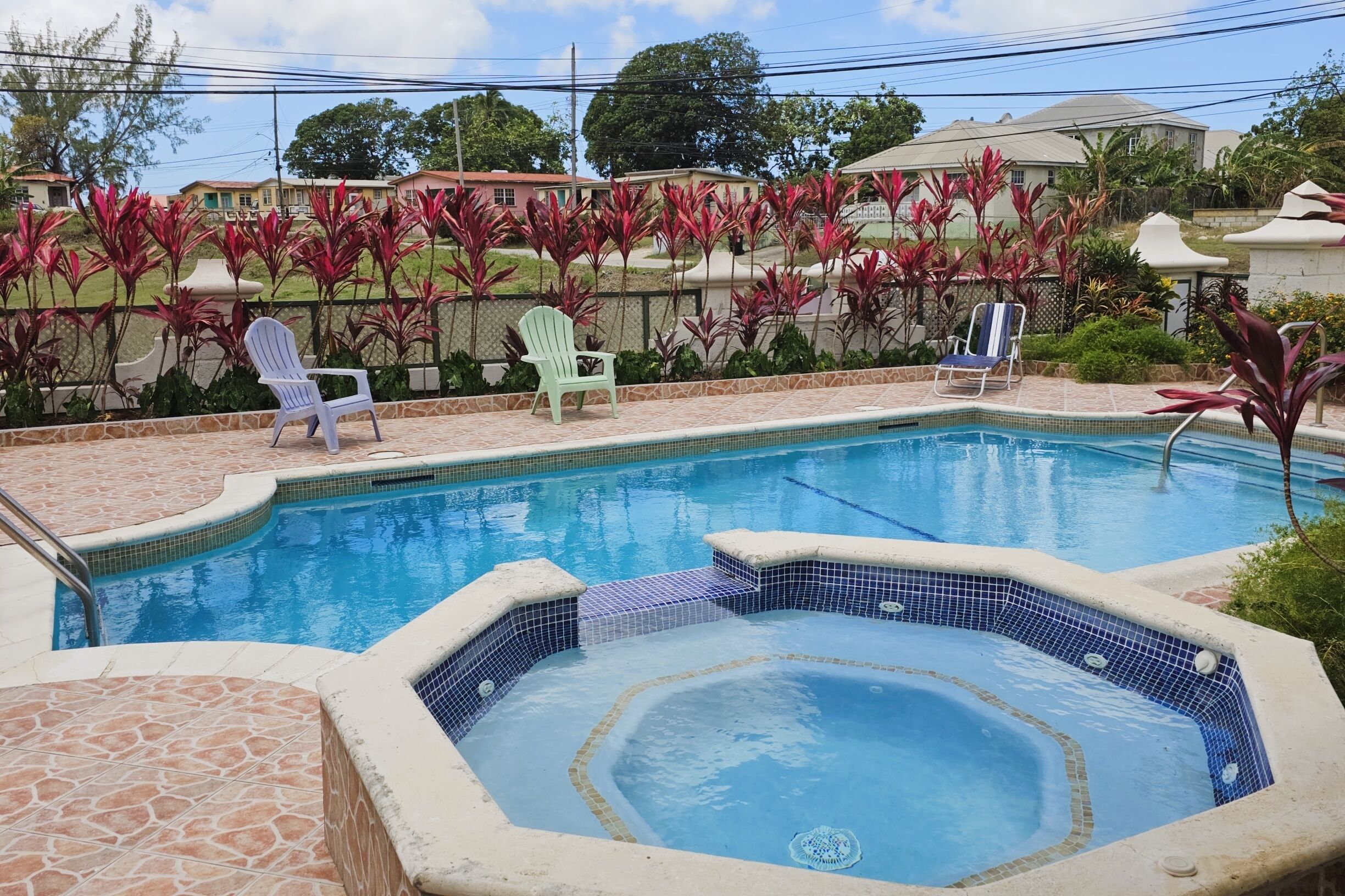 A swimming pool with a hot tub, surrounded by chairs and plants.