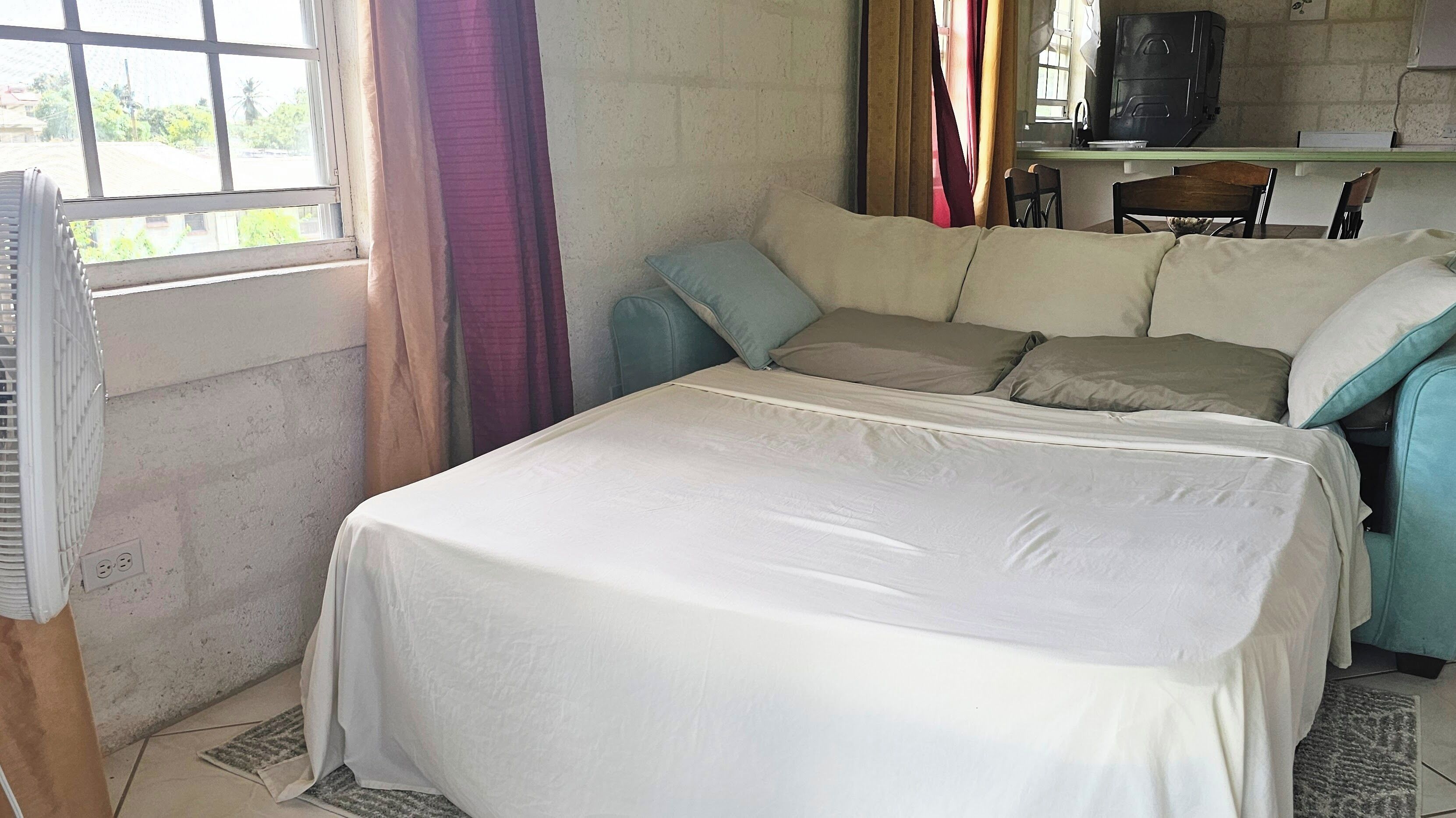 A single bed with a white bedspread in a room with a window, a chair, and a small table.