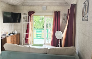 A room with a TV, a wooden cabinet, a sofa, a fan, and a window with curtains.