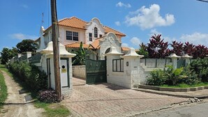 A large, two-story house with a tiled roof, a gated entrance, and a paved driveway. - Jackson Breezy Vacation and Venue Rental Barbados (Canewood)
