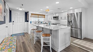 A modern kitchen with white cabinetry, stainless steel appliances, and a central island with bar stools.