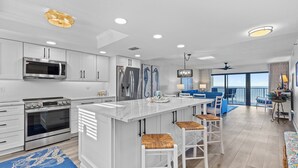 A modern kitchen with white cabinetry, a large island with bar stools, a built-in oven, and a microwave.