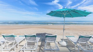 A beach with white lounge chairs and a green umbrella.